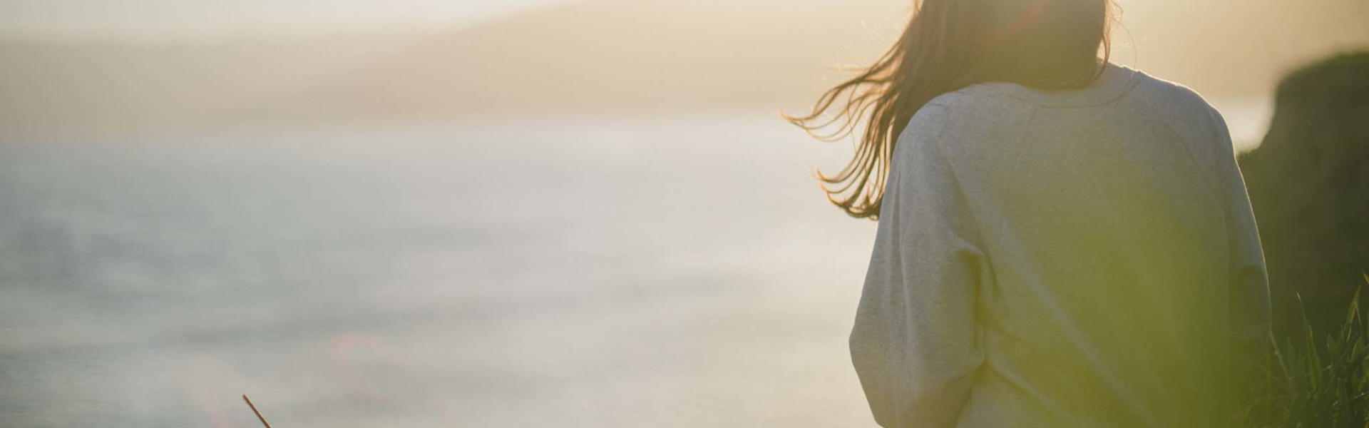 cinclus pharma brown haired woman sitting on cliff watching sunset over the ocean